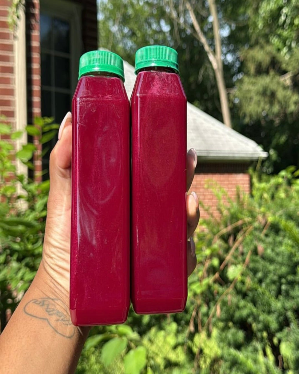 Hand holding two bottles of Kae Health Juice cold pressed beet juice with green caps outdoors