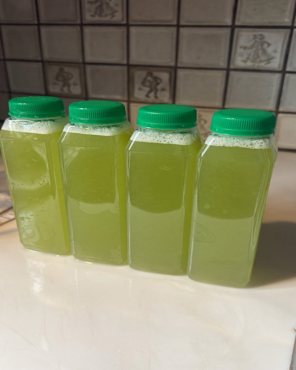 Four bottles of Kae Health cold pressed honey dew juice with green caps on a kitchen counter