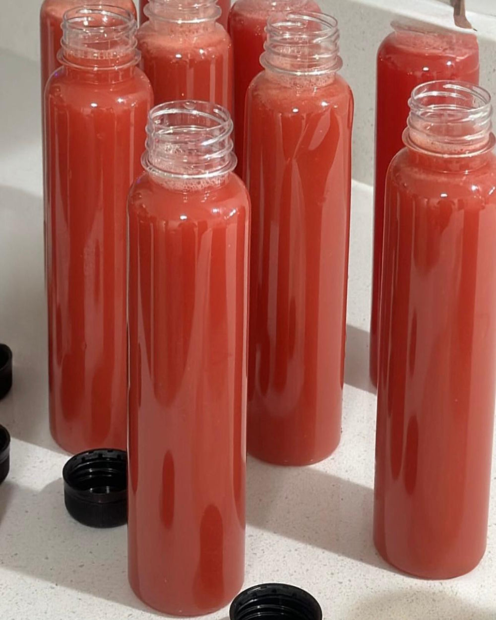 Bottles of vibrant red watermelon mojito juice by Kae Health Juice with black caps on the side